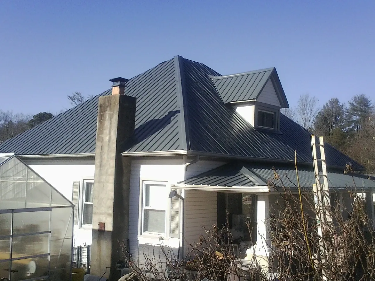 Dark blue standing seam metal roof on a white farmhouse with dormer — Slate & Tile Roof Repair by Roofing Brothers in Blue Rapids