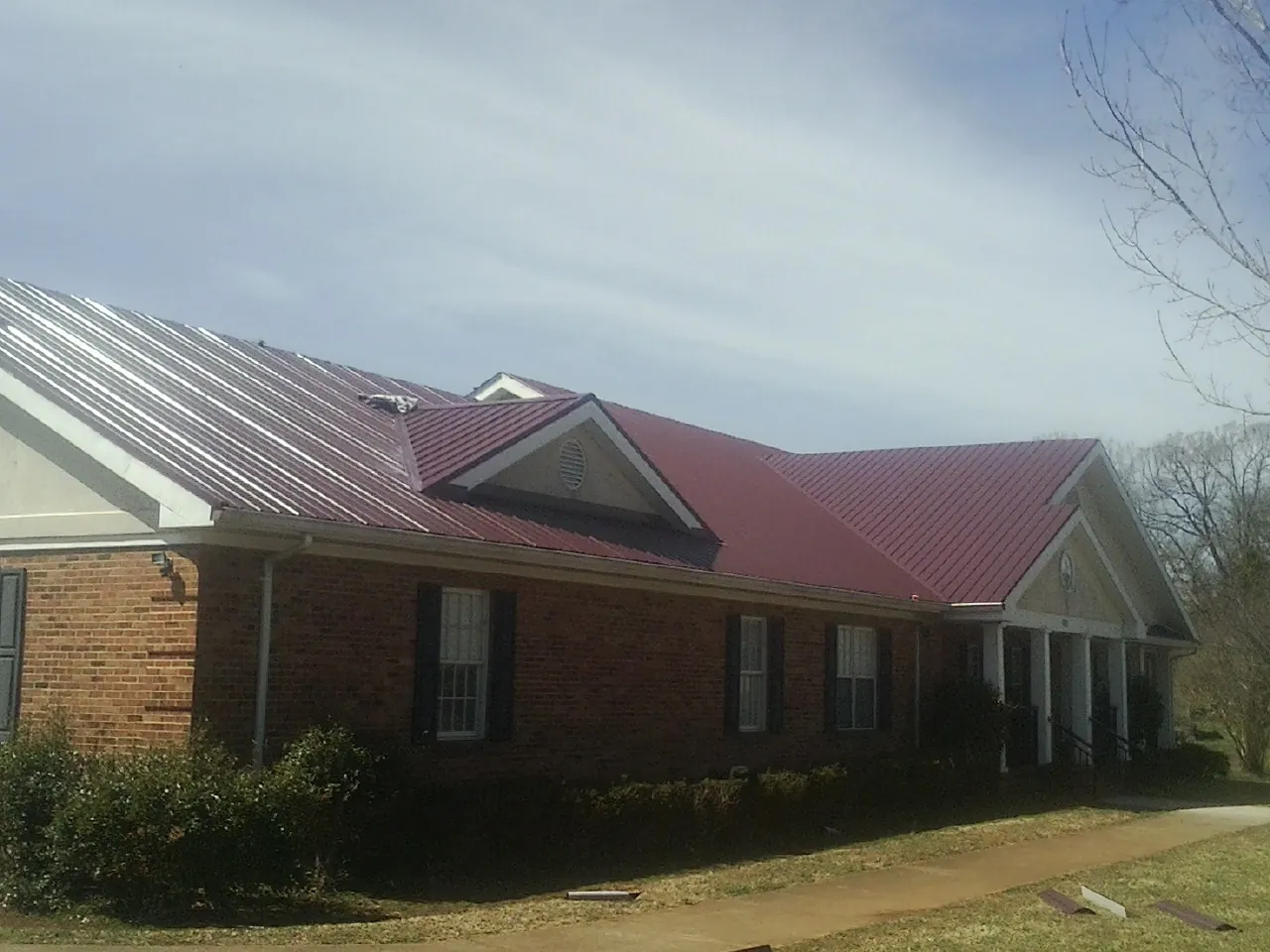 Red metal roof with gabled entries on a long brick building, from a Hail Damage Roof Repair job in Blue Rapids