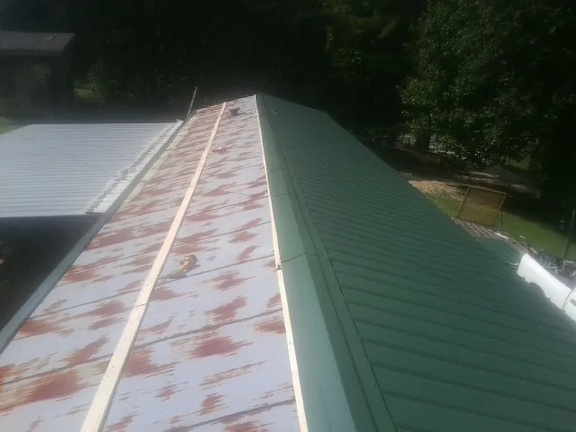 Old rusted panels beside newly installed green metal roofing — Wind Damage Roof Repair by Roofing Brothers in Blue Rapids