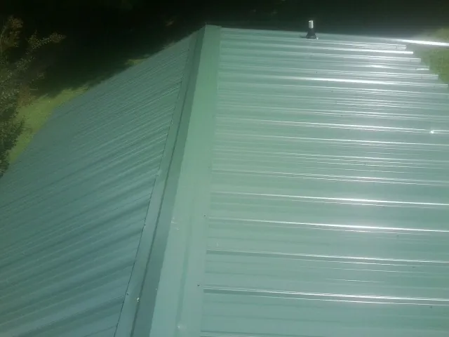 New green metal panels meeting at the ridge of a roof — Flat Roof Repair work by our crew in Blue Rapids