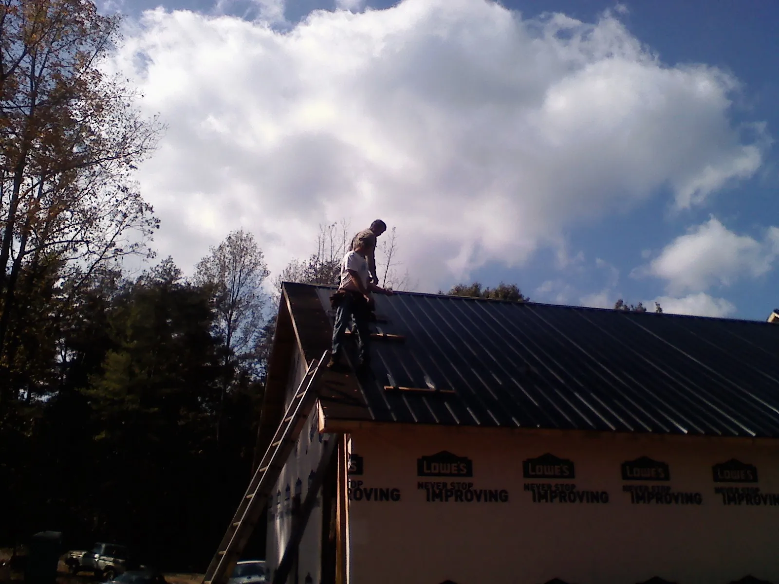 Roofer fastening dark metal panels high against a cloudy sky, from a Roof Inspection job in Blue Rapids