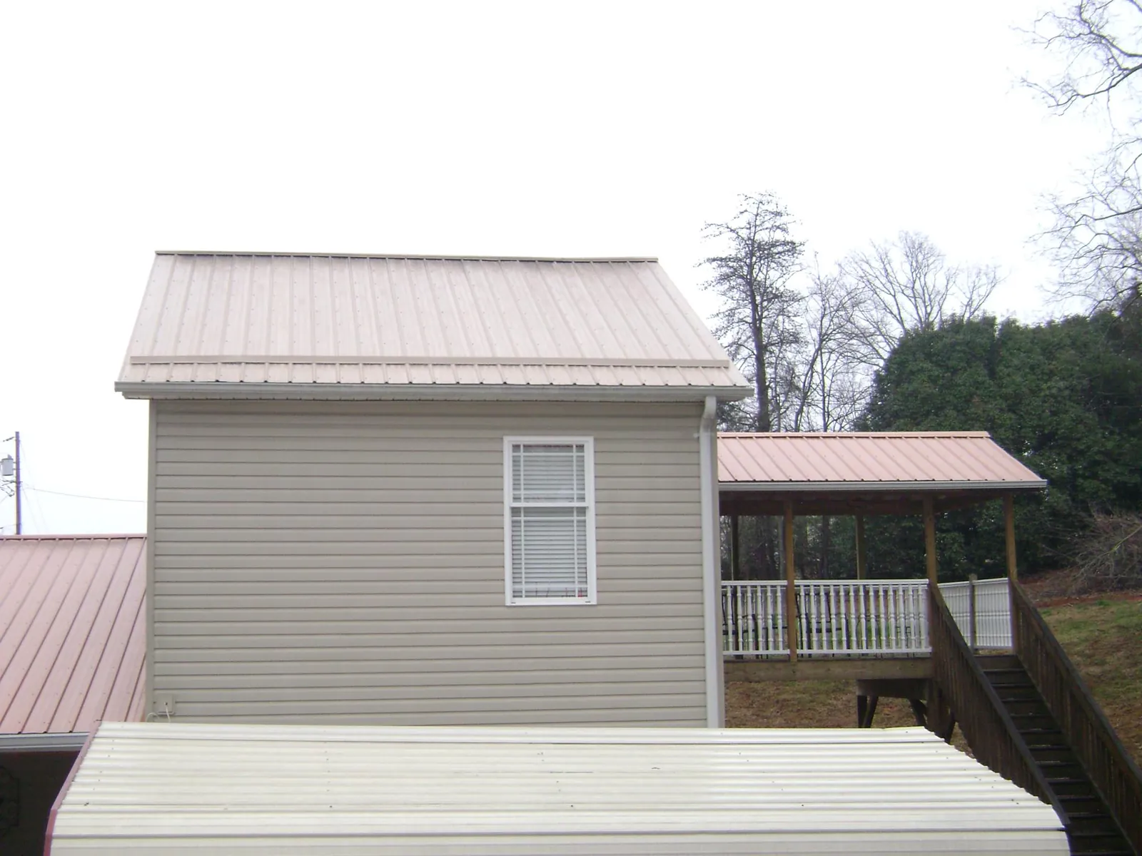 Tan metal roofs on a two story addition and attached porch, from a Roof Replacement job in Blue Rapids